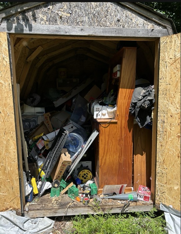 Storage shed before cleanout, packed floor to ceiling with boxes and debris