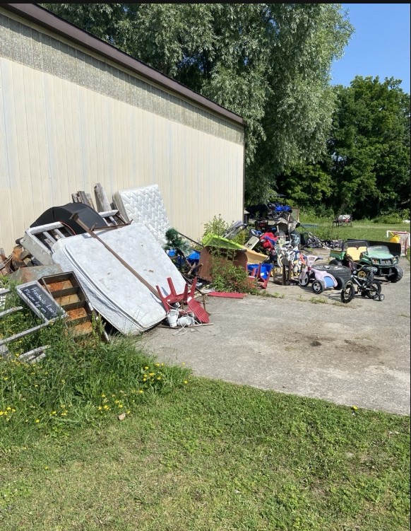 Property side yard before cleanout, piled with mattresses, furniture and toys